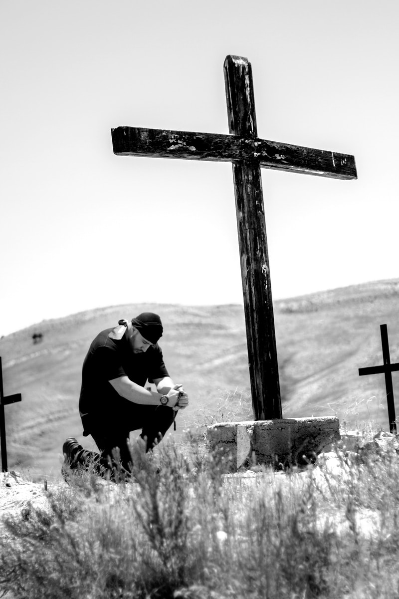 man kneeling in front of wooden cross