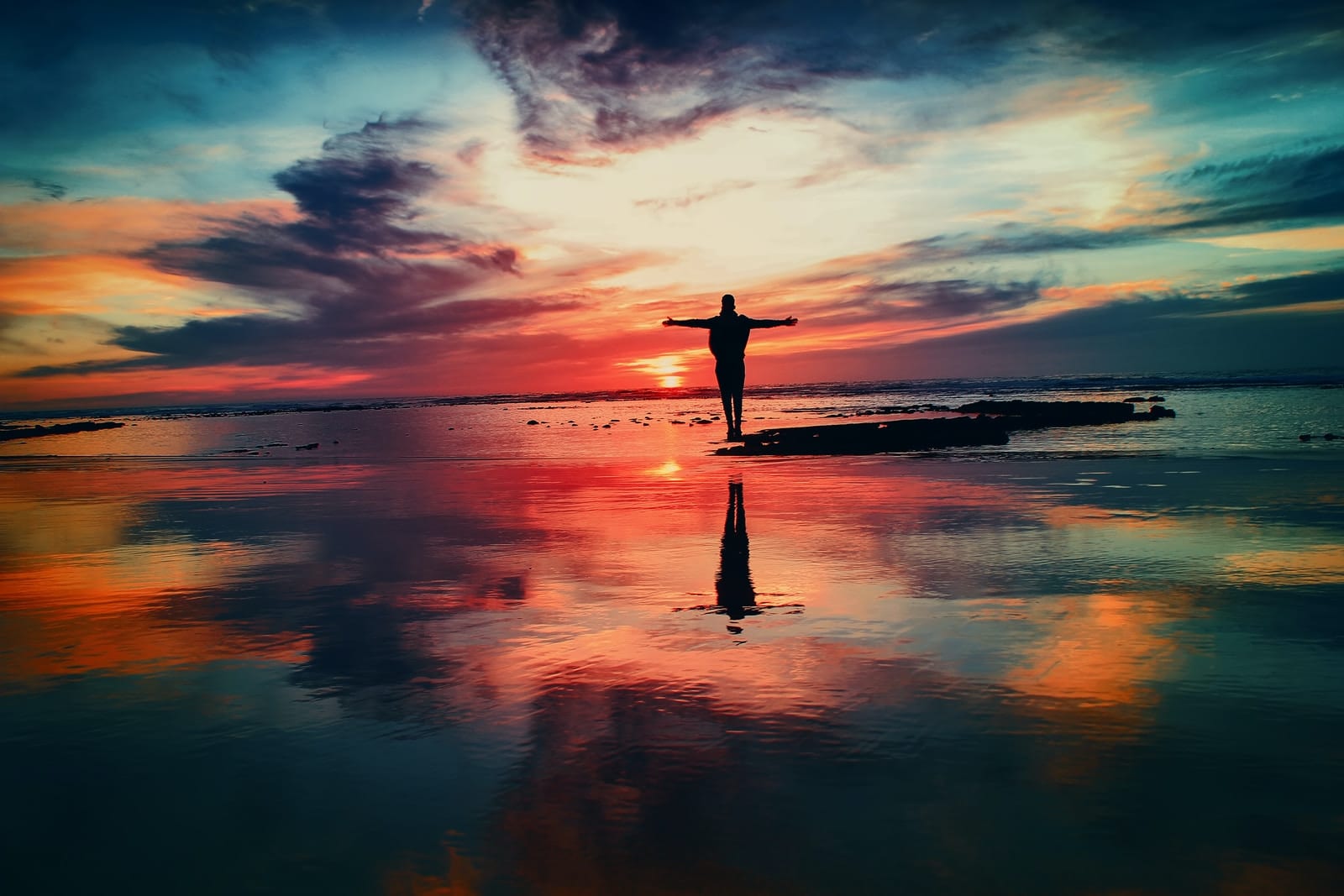 Photo by Mohamed Nohassi silhouette of person standing on rock surrounded by body of water