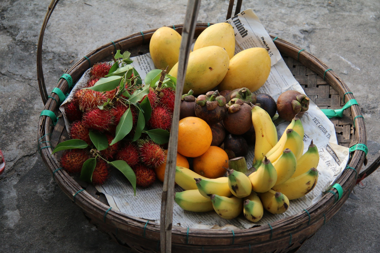 basket of yellow bananas, yellow mangoes, red rambutan fruits, oranges, and mangosteen fruits